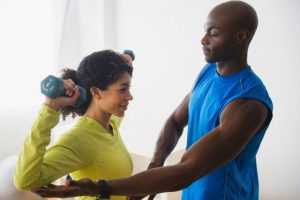 Woman lifting weights with trainer in gym